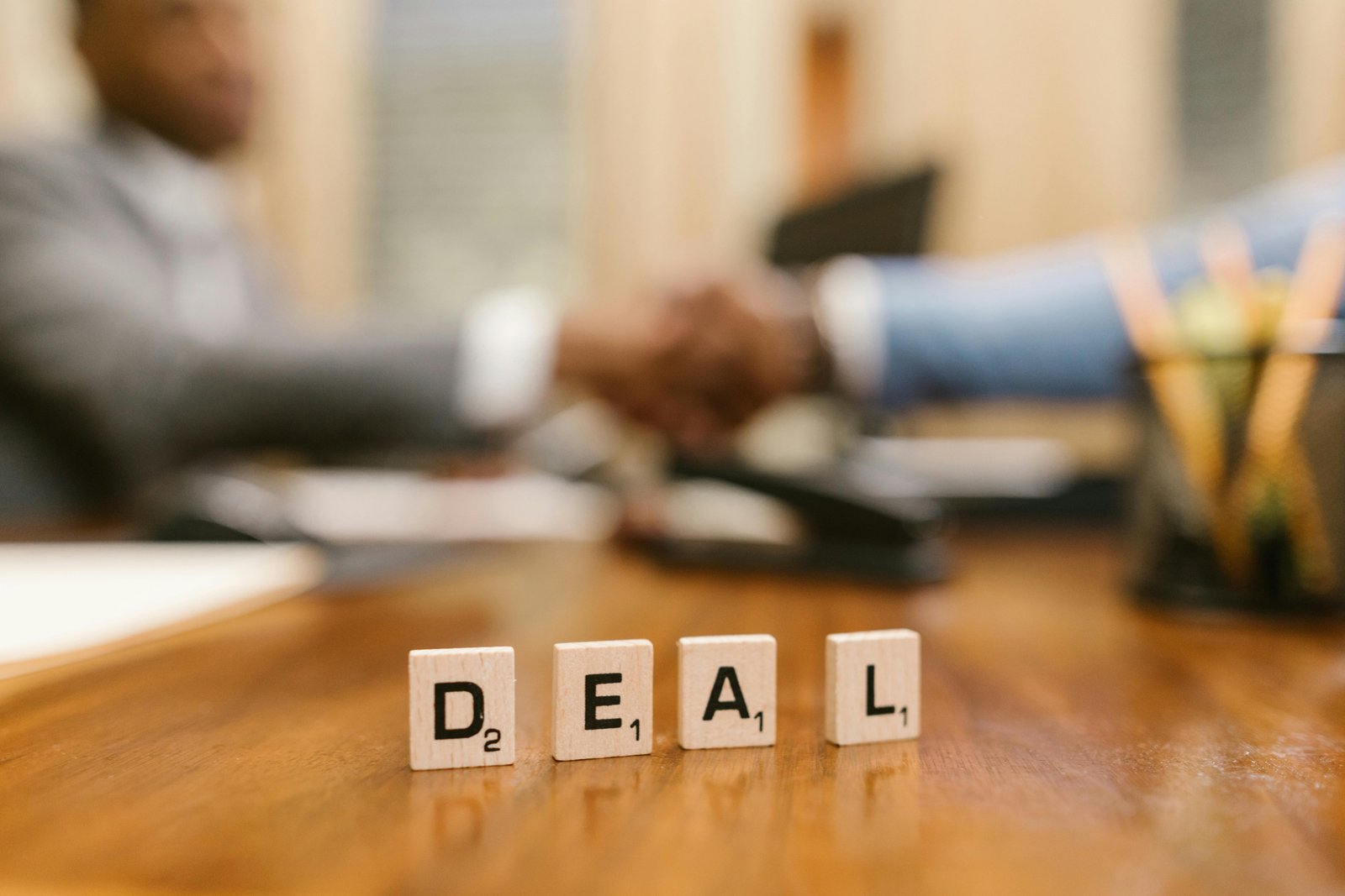 Close-up of Scrabble tiles spelling 'deal' with a handshake in the background.